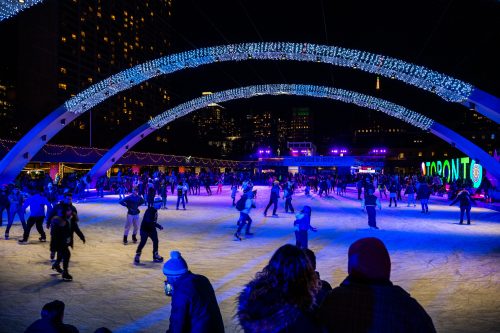 People skating in outdoor rink with lights overhead.