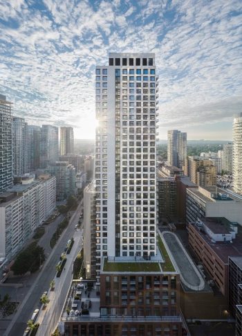 A tall apartment building with many square windows and a blue sky with clouds in the background.