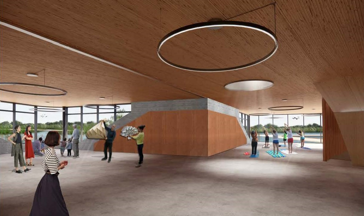 Rendering of the flexible use spaces in the recreation building. The open-plan, L-shaped interior has concrete floors, wood finishes with grey masonry accents and several large circular lights hanging from the ceiling. People are depicted participating in various community group activities, demonstrating different uses for the space. Floor-to-ceiling windows at both ends provide views of a terrace, pond and trees.