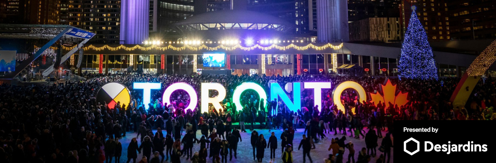 Night scene of skaters on rink in front of colourful Toronto sign, Christmas tree and City Hall. Presented by Desjardins in bottom right corner.