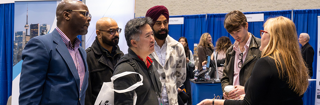 Group of people in a trade show setting listen to a person speak