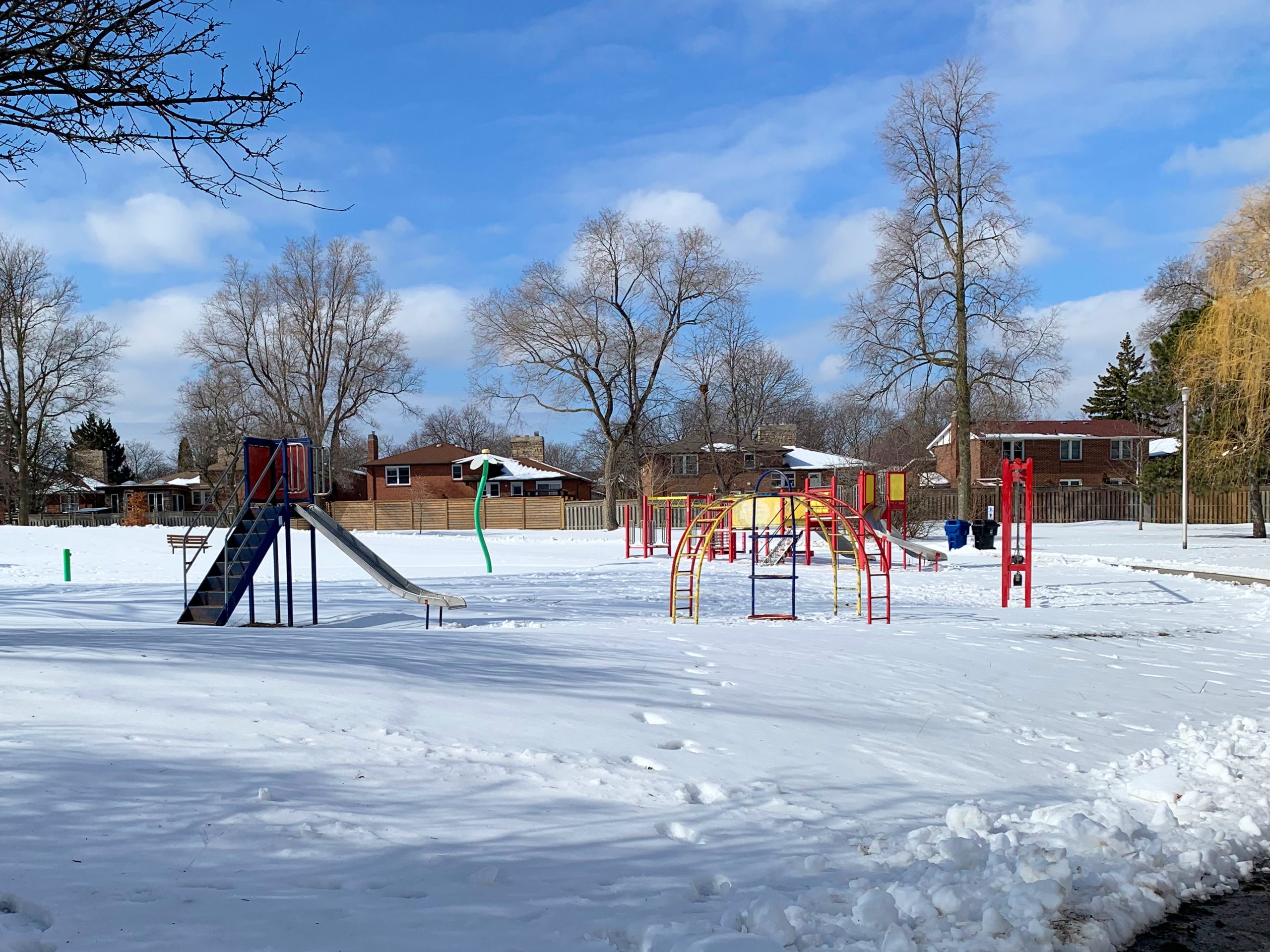 Stephen Leacock Park playground before construction looking west from the existing walkway. The playground is surrounded by a splash pad, open lawn space and residences in the background.