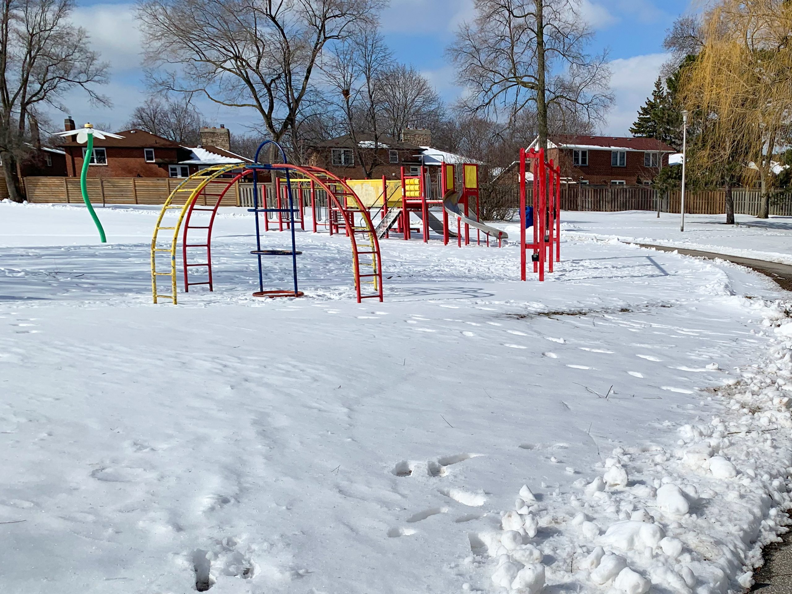 Stephen Leacock Park playground before construction looking south-west from the existing walkway. The playground is surrounded by a splash pad, open lawn space and residences in the background.
