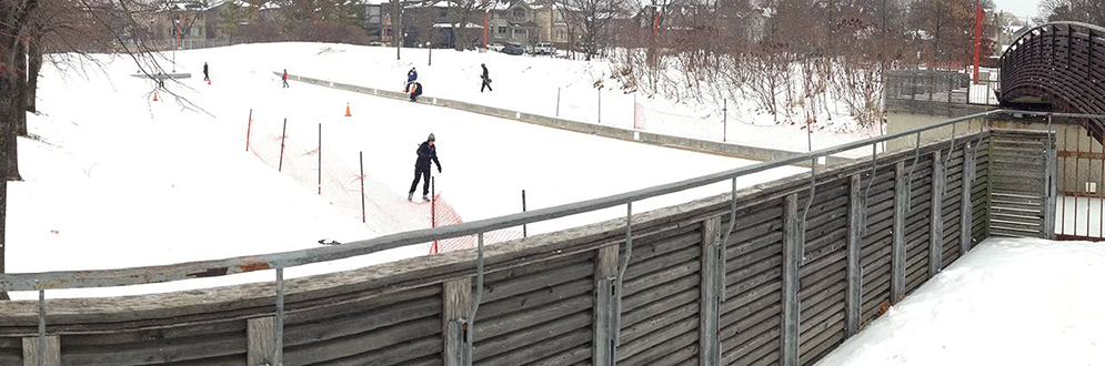 People skating on an outdoor ice rink in winter as seen from the bridge.