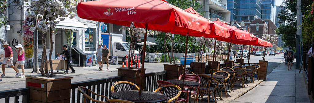 A restaurant patio with red umbrellas, tables and chairs.