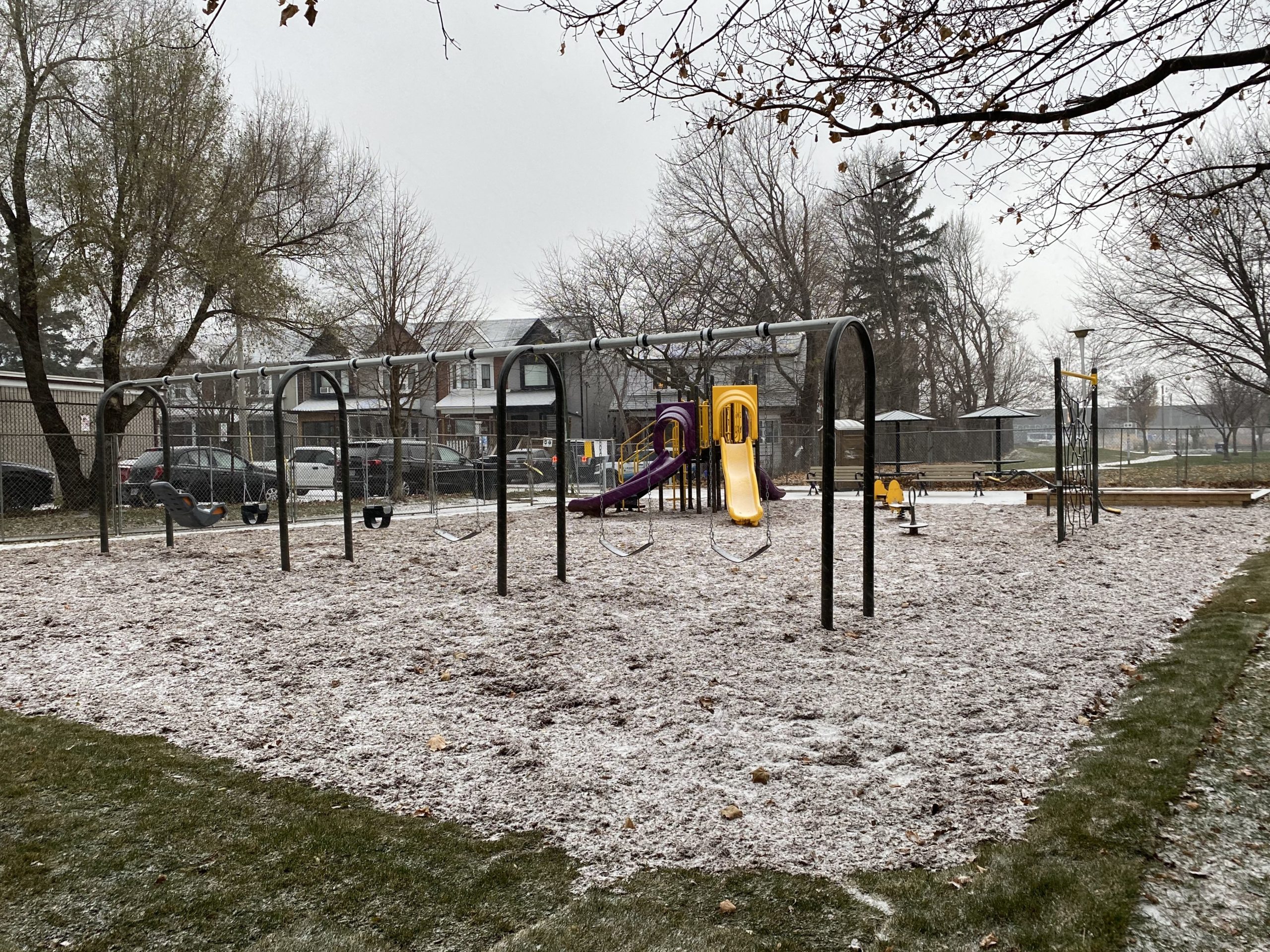 S.A.D.R.A. Park playground with a swing-set in the foreground, the play structure with purple and yellow slides in the background and the spider climbing-net to the left.