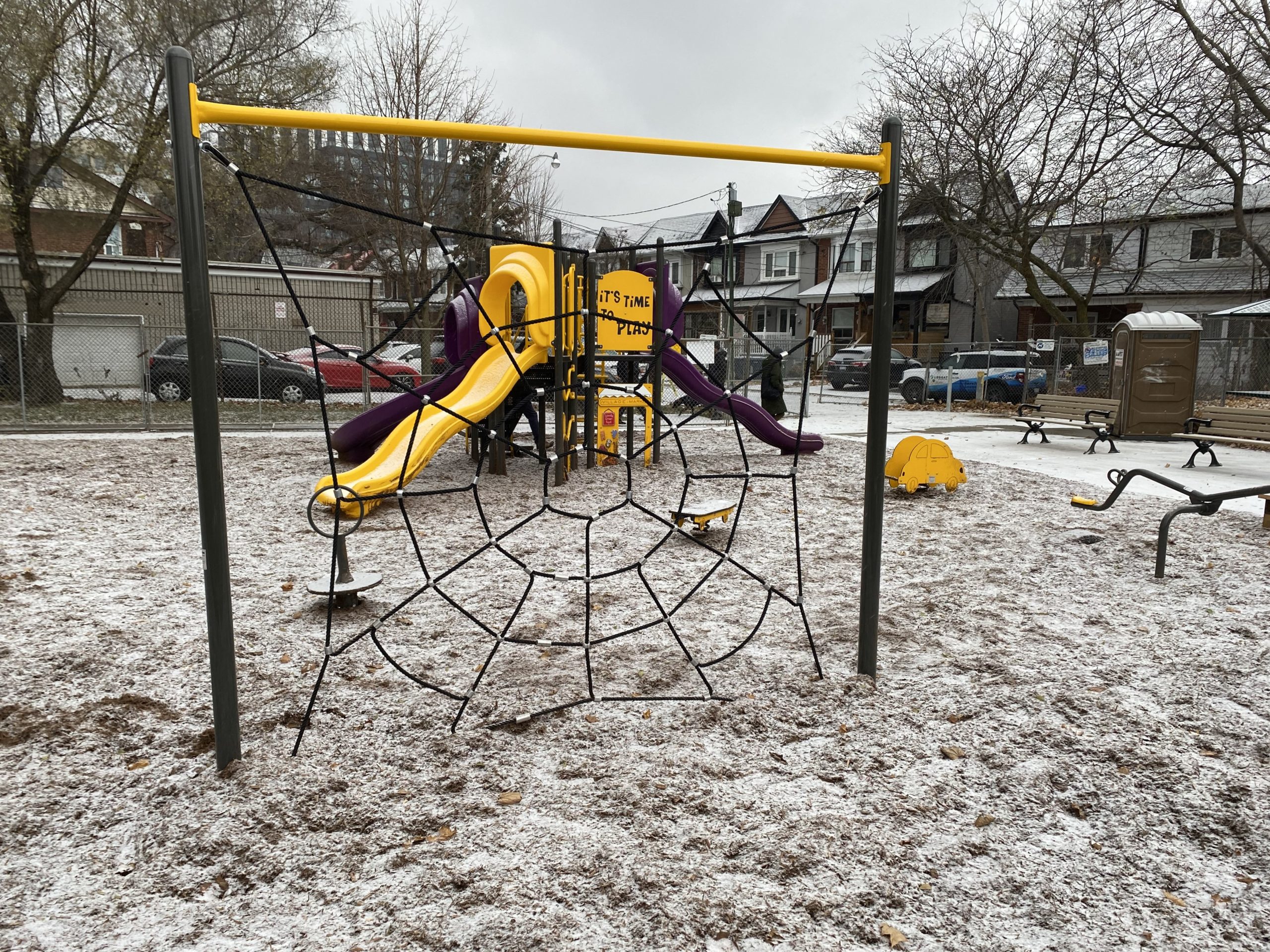 S.A.D.R.A. Park playground with the spider climbing-net in the foreground, the yellow and purple play structure in the background, and, the spring toy and teeter-totter to the left.