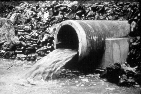 A sewer pipe with water spilling out of it. 