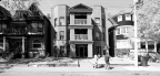 A small-scale apartment on a street with two people walking by it.