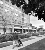 A man walking a stroller down the sidewalk in front of a mixed-use apartment building.