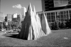 Large art sculptures outside on grass in front of a bench with a man sitting on it.