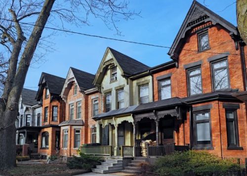 Row houses in varying shades of red, green and blue brick with a blue sky in the background.
