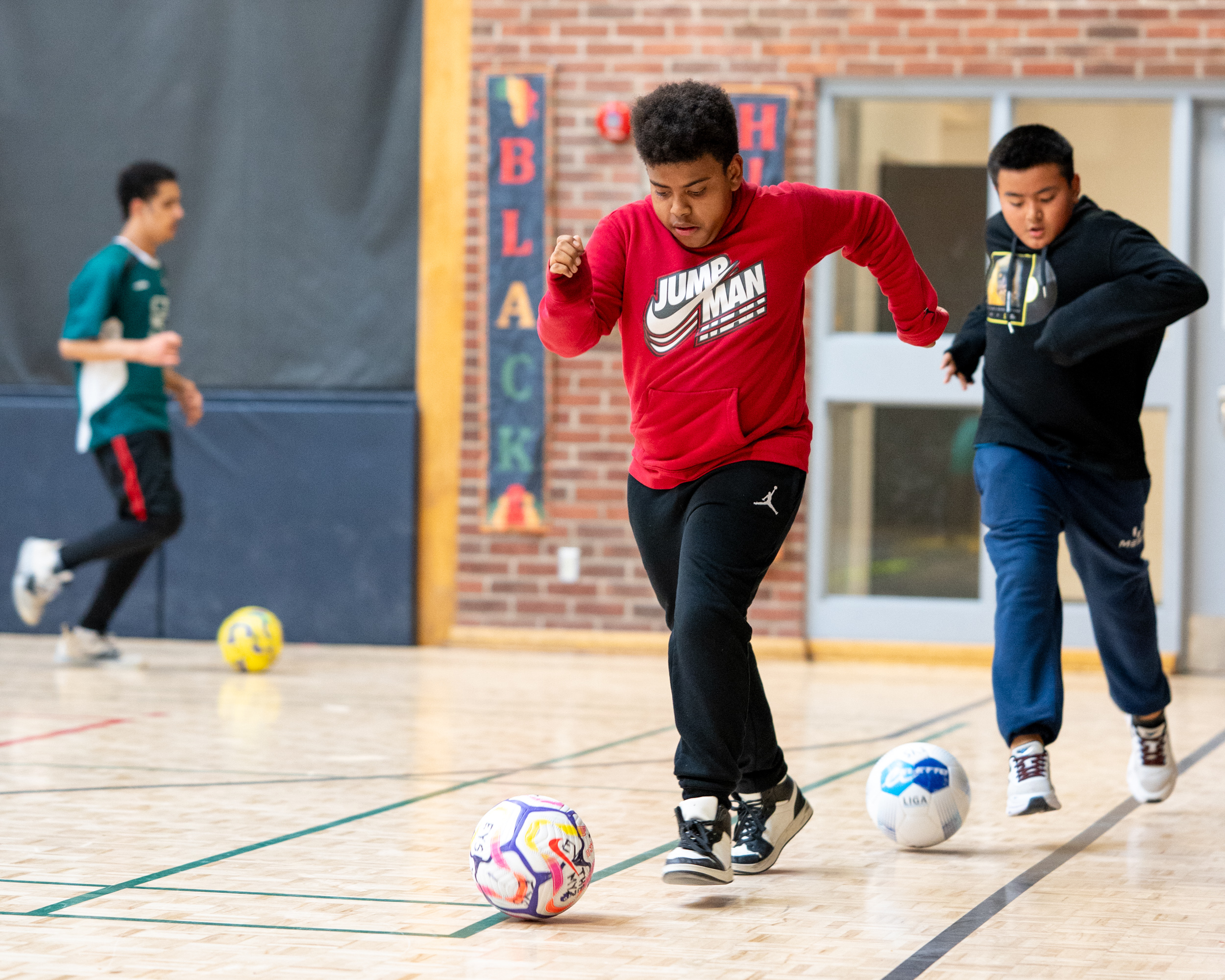Three youth running participating in a soccer drill at Masaryk-Cowan Community Recreation Centre at an “Improving Well-Being Through Sport” workshop.