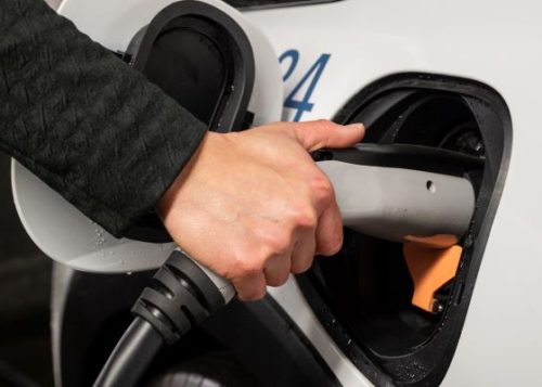 A person's hand holding an electric vehicle charger and plugging it into a City fleet electric vehicle.