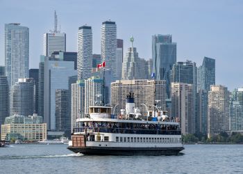 Toronto Island Ferry flying a Canadian flag on Lake Ontario with blue skies and city buildings in the background.
