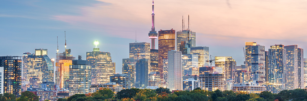 View of downtown Toronto skyline looking over trees towards the CN Tower. The sky is pink at sunset.