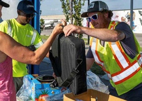 A person handing a laptop bag over to another person wearing a reflective vest for a community environment days drop-off.