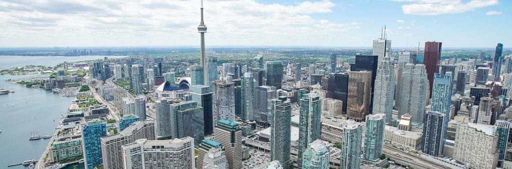 An aerial view of the CN Tower and city buildings on a sunny day with the waterfront in background.