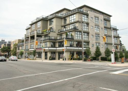 A mid-rise beige building with balconies and different levels at a traffic intersection.