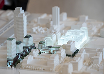 A model of miniature white and black city buildings with lights shining from the black buildings.