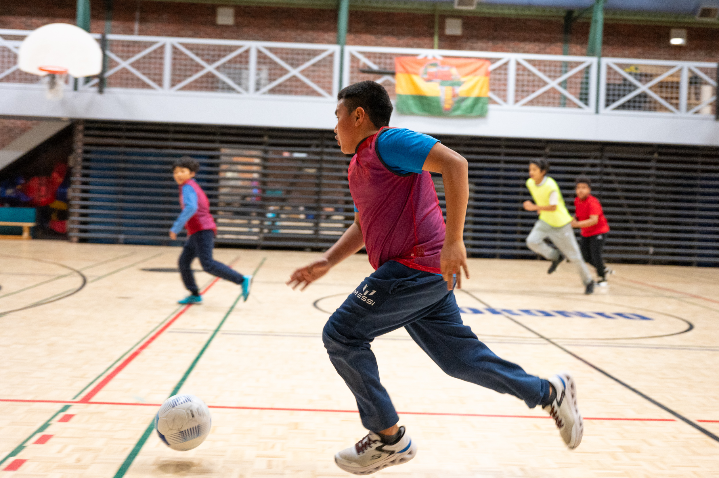Group of youth playing soccer in the gymnasium at Masaryk-Cowan Community Recreation Centre at an “Improving Well-Being Through Sport” workshop.