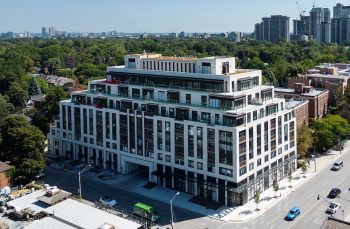 Mid-rise building, white and black building in the corner with trees in the background.