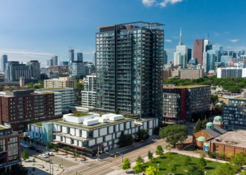 A mix of low-rise, mid-rise and high-rise buildings in Toronto with a blue sky and the CN Tower in the background.