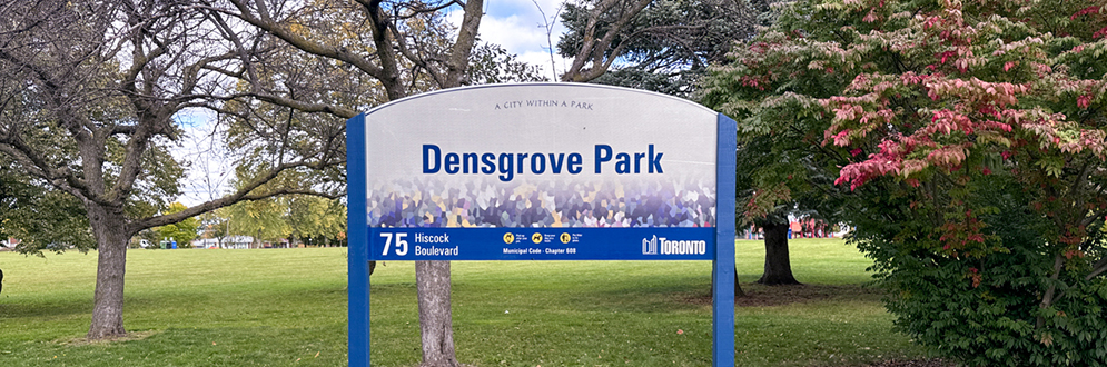 The park sign in front of a grassy greenspace with trees.