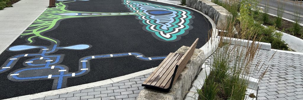 image of an intersection near Raindrop Plaza (Coxwell Avenue and Dundas Streeet East) It shows a vibrant landscape with benches and street art.