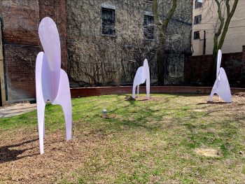 Grassy area with three eerie figures, not human, not animal constructed from metal