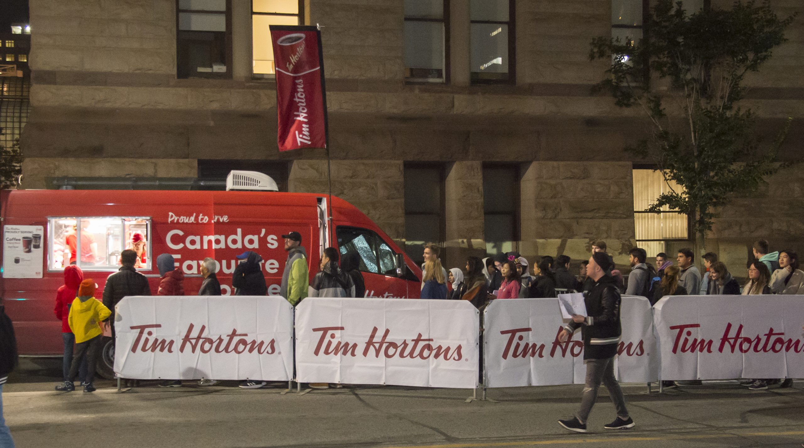 Large crowd lines up at the Tim Hortons truck where staff serve hot beverages beside branded signage and banners.