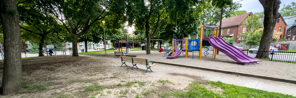 A playground with a bench in the foreground and surrounded by sand.