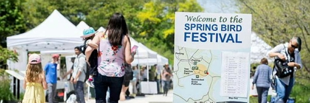 White tents set up along a path with trees in the background and a sign that reads Welcome to the Spring Bird Festival in the foreground.