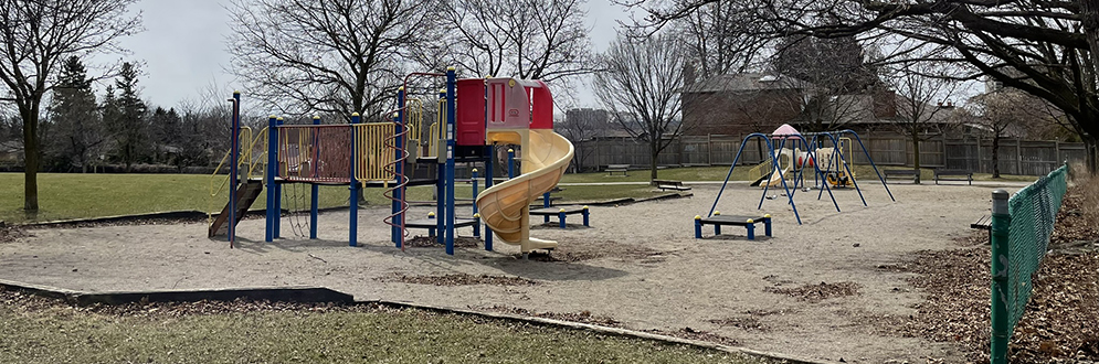 Gulliver Park Playground showing a large play structure in the foreground with a curved slide and a swing set and small play structure in the background. The playground is on top of sand and surrounded by grass.