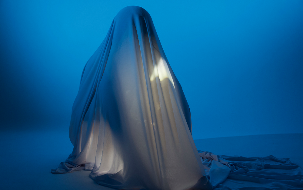 Sitting figure draped in a white cloth against a blue background.