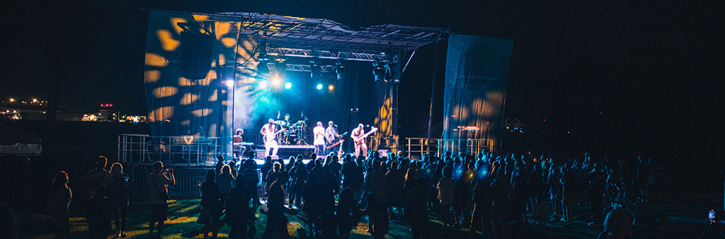 A band play outdoors at night in front of a standing crowd.