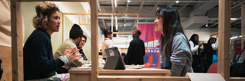 2 people sit face to face at a table chatting with others doing the same in the background.
