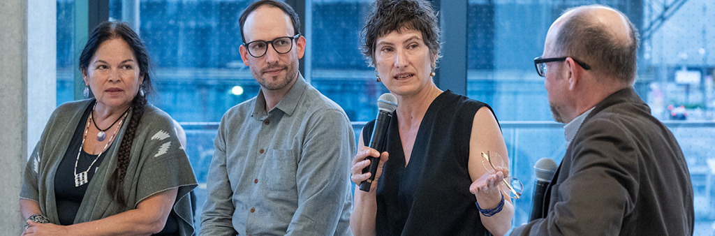 One person speaks into microphone while three other panelists listen.