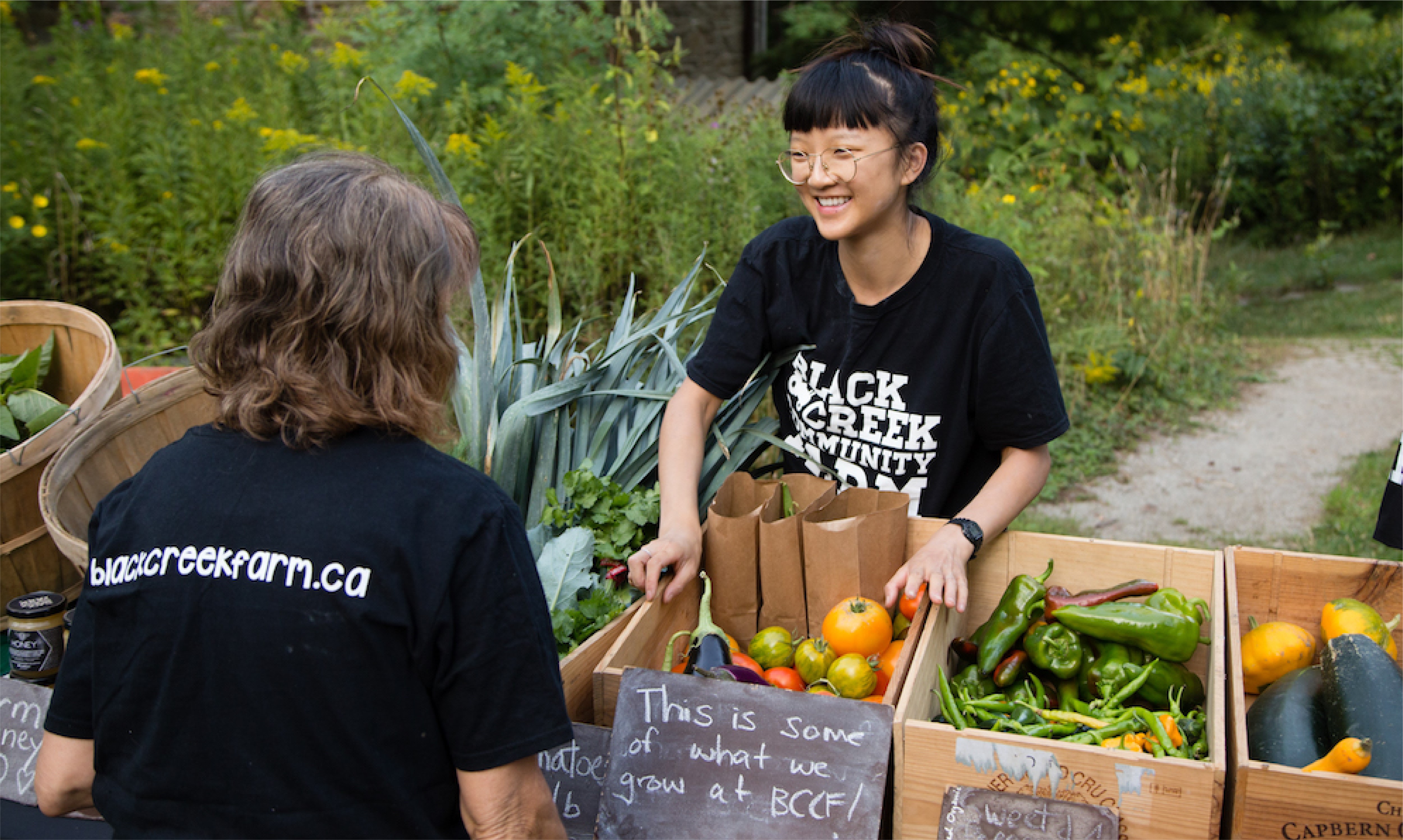 A women standing behind a table with boxes filled with fresh food speaking with a customer.