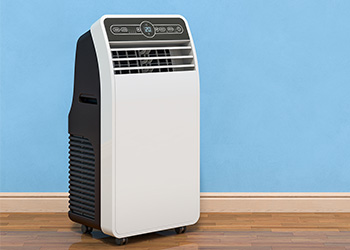 A portable air conditioner sitting on the floor in front of a blue wall.