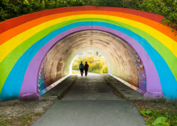 Two people walking underneath a rainbow tunnel.