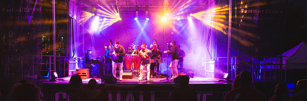 A band playing on a stage outdoors at night with brightly coloured stage lights.
