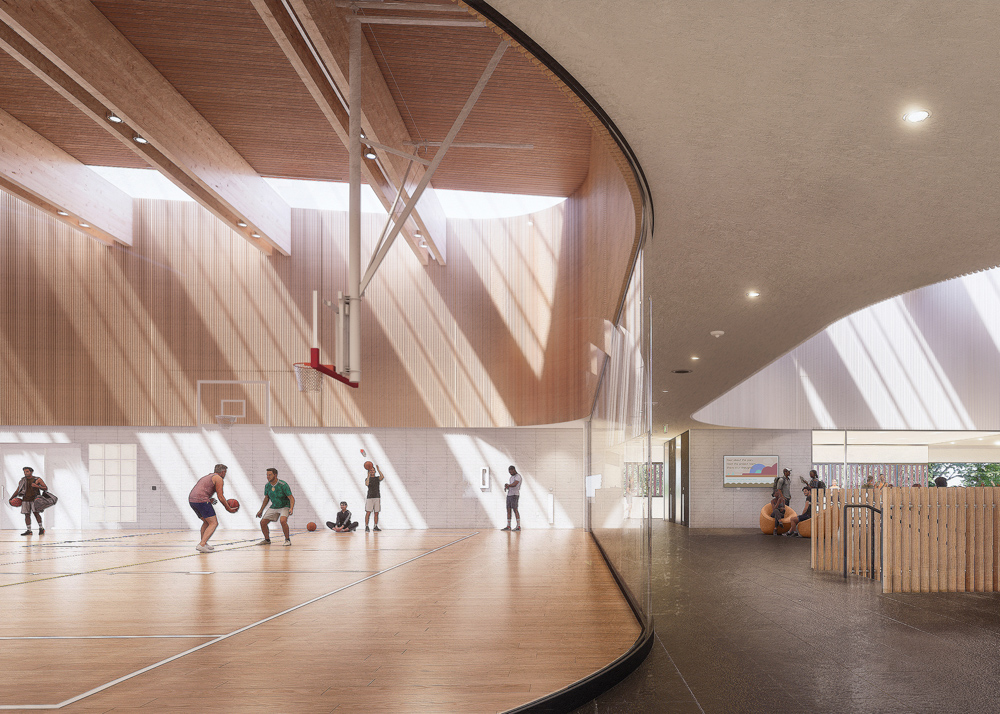 Rendering of the gymnasium and adjacent lounge in the community centre. The gymnasium features a high wooden ceiling with beams and skylights. Basketball hoops are suspended from the ceiling, and people are shown playing basketball on the wooden court. A curved transparent wall separates the gymnasium from a passageway, which connects to a set of stairs and a small seating area in the lounge.