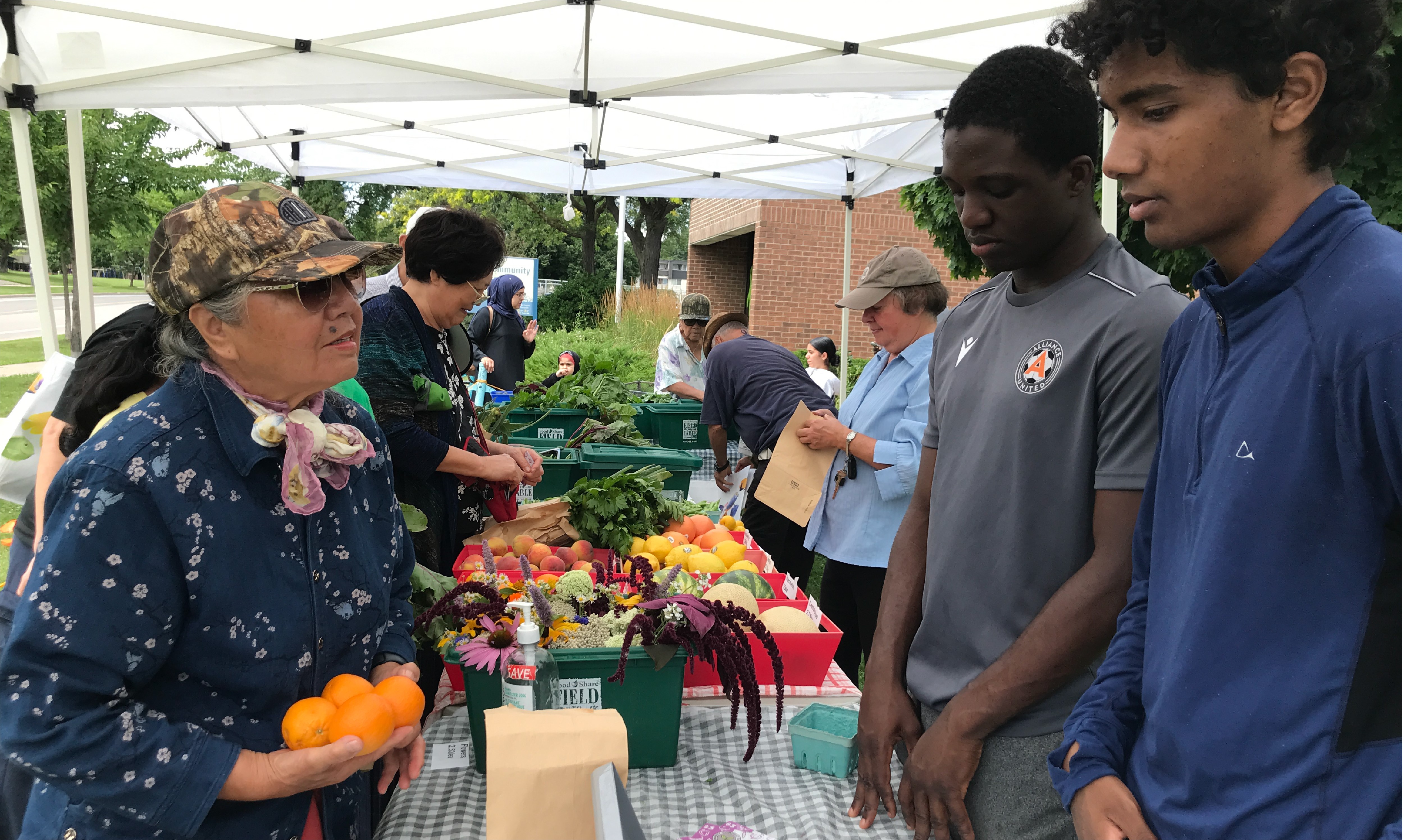 People picking up fresh produce from a tented table.