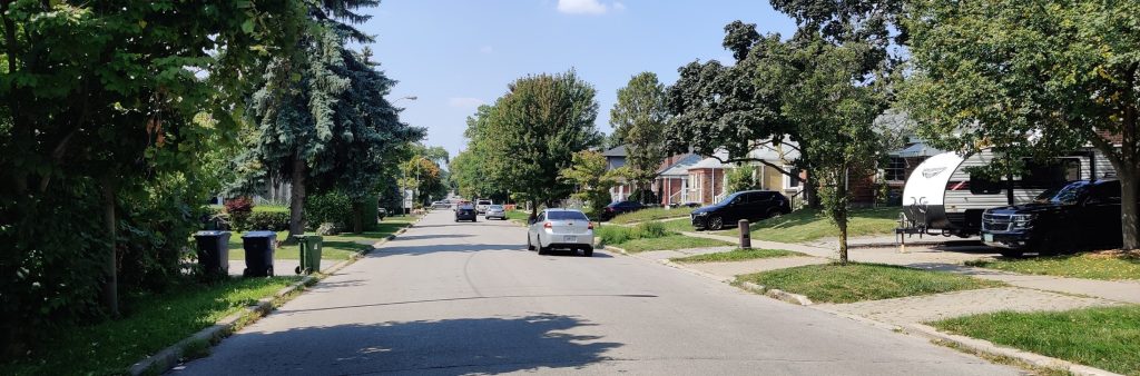 View of Hendon Avenue, looking west from Kensington Avenue, showing a tree-lined street, with a few cars in the distance.