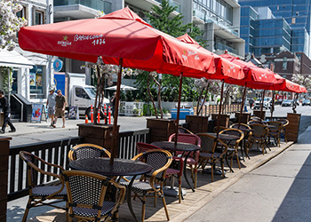 An outdoor restaurant patio with red umbrellas, tables and chairs.