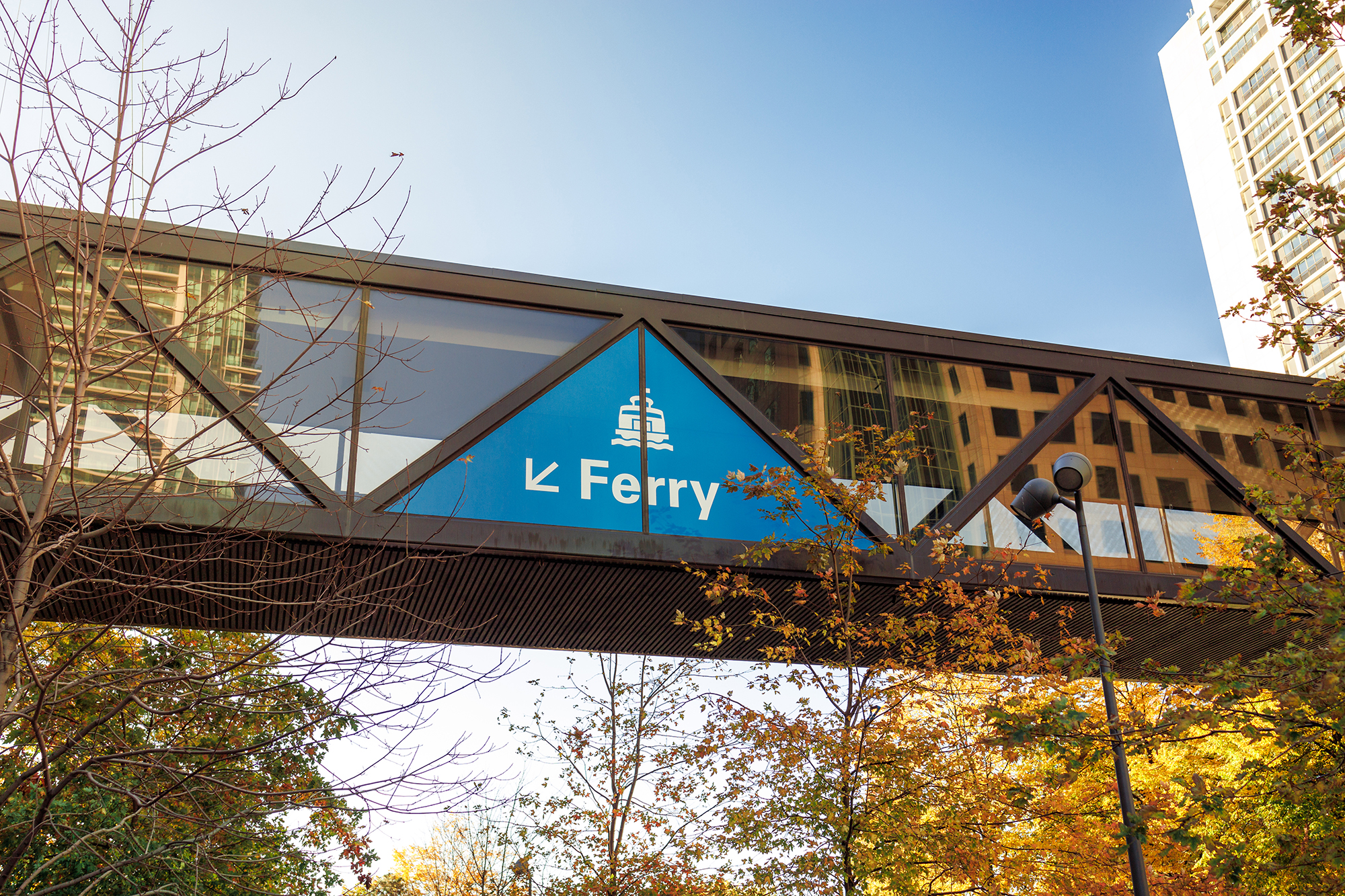 A large triangular blue sign pointing to the ferry terminal is located on an overhead pedestrian bridge at the entrance to the Jack Layton Ferry Terminal.