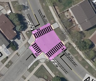 An aerial image of the intersection of Alton Towers Circle and Ingleton Boulevard highlighting the entire intersection in mauve. Lines are drawn on the road to show curb extensions on the side of Ingleton, crosswalks on all three sides of the intersection and adjusted lines on the road. 