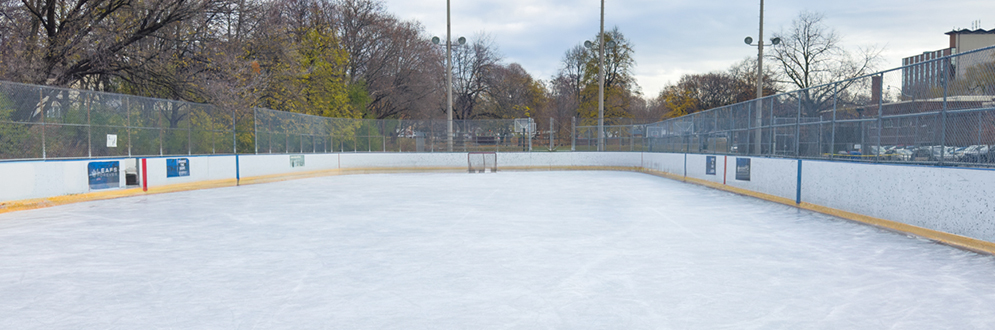 An outdoor ice rink with a board barrier around the edge. A hockey net is at one end.