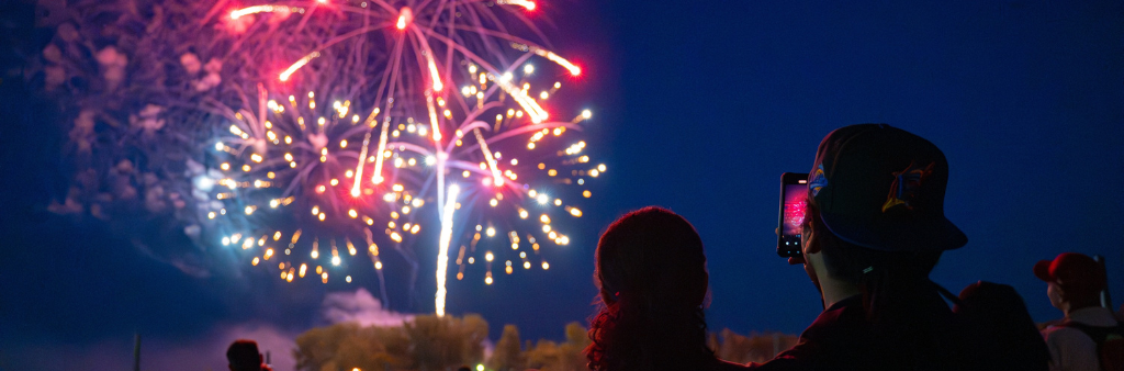 Backs of people looking at and taking photos with their phones of fireworks